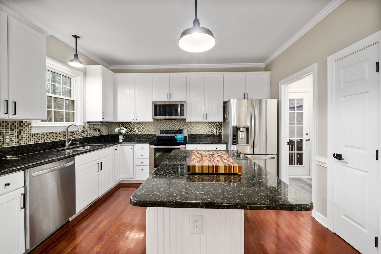 Spacious modern kitchen featuring white cabinets and black granite countertops with stainless steel appliances.