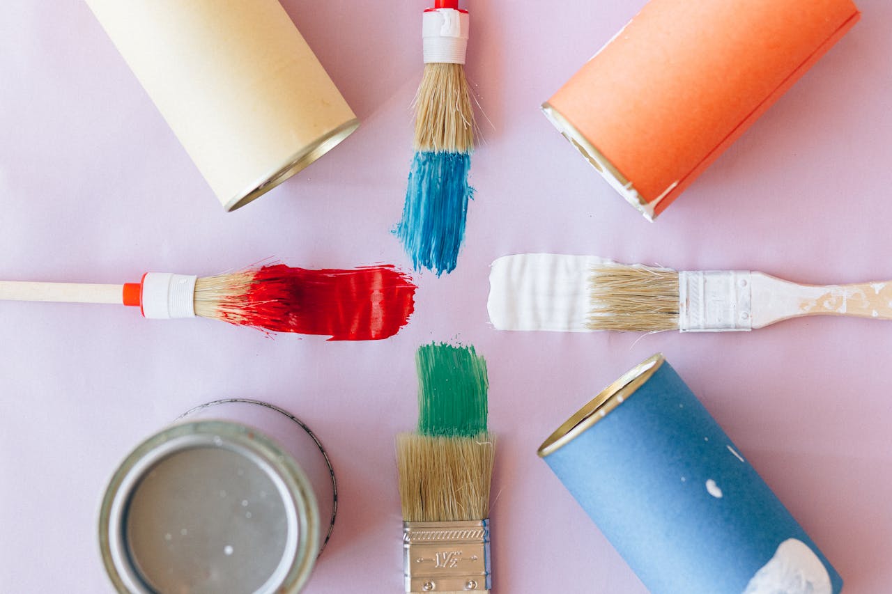 about-06 Top view of vibrant paintbrushes and cans against a pastel backdrop, ideal for creative projects.