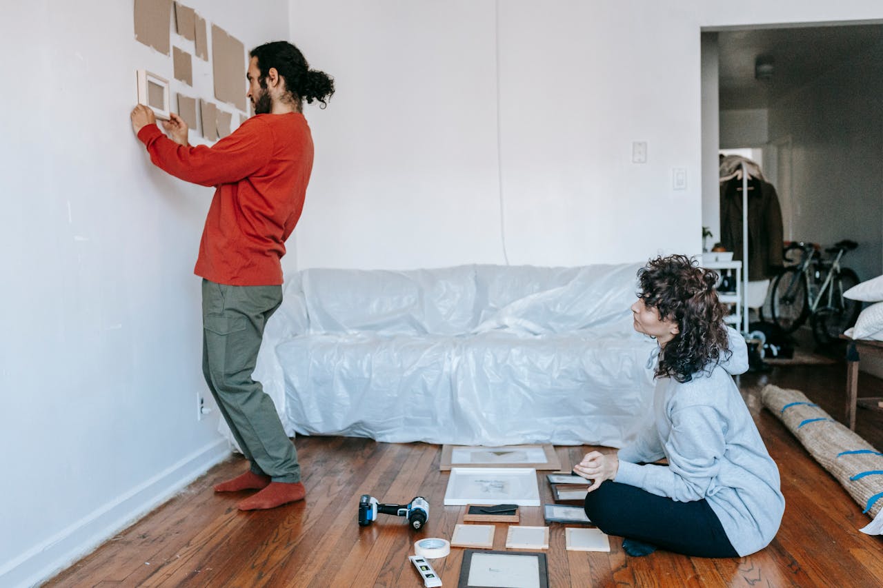about-07 A couple decorates their new home living room by arranging picture frames on the wall.